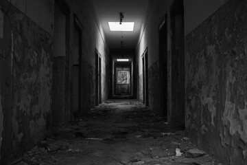 A hallway in an abandoned building with crumbling walls and rubble and a window through which light comes in