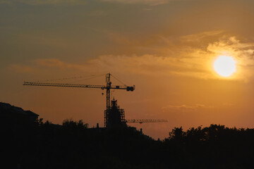The setting sun with an orange sky and silhouettes of trees and cranes in Timisoara, Romania