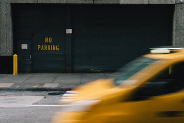 A vibrant yellow taxi is speeding past a prominently displayed no parking sign
