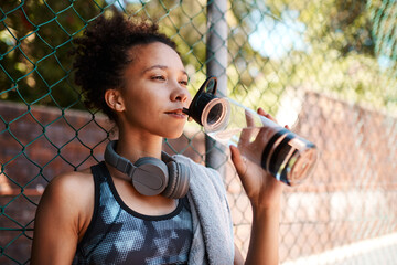 African woman, fitness and drinking water outdoor for health, diet and wellness on break by fence....