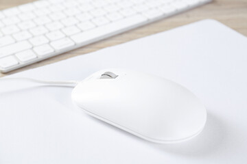 White computer mouse with mousepad and keyboard on wooden table, closeup