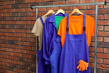 Different workers' uniforms on clothing rack near brick wall