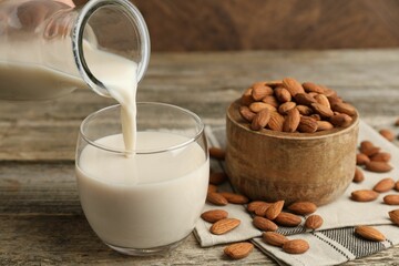 Pouring almond milk into glass and nuts at wooden table, closeup