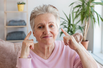 senior woman pointing finger at her ear, looking at camera and smiling