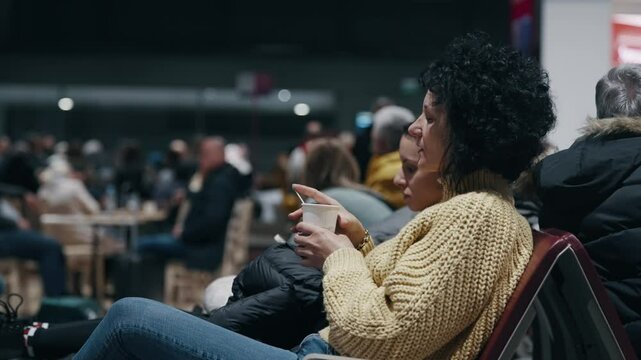 A woman relaxes with a coffee in a busy airport waiting area during a flight delay in Cologne, Germany. The scene captures travel stress and the calm amid chaos. Cinematic isolated shot