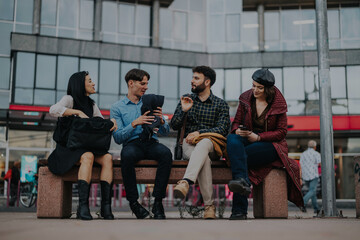 Fototapeta premium A group of young professionals engaging in a lively conversation while seated on a bench in an urban environment. They appear casual and relaxed, suggesting a moment between business activities.