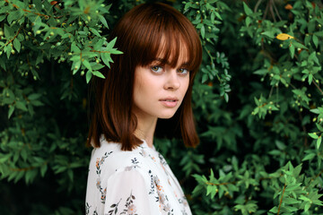 Portrait of a redhaired woman standing among lush greenery with intense gaze