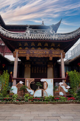 A traditional Chinese building in Shanghai features intricate wooden carvings and a curved roof with dragon motifs, surrounded by greenery and flowers. © Aerial Film Studio