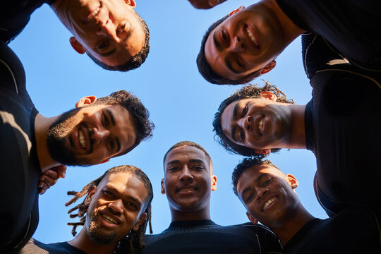 Portrait, people and outdoor rugby team in circle, low angle solidarity and group for sports. Men, blue sky and professional athletes together for training, practice and fitness unity at competition
