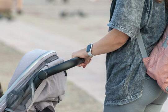 A woman is pushing a stroller with a baby in it. She is wearing a watch and a grey shirt