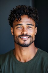 Obraz premium A confident man with curly hair, sporting a well-groomed beard, smiles warmly in a studio shot, exuding charm and friendliness with an artistic touch.