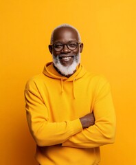 An elderly man with glasses and a white beard smiles warmly, dressed in a yellow hoodie, standing against a matching yellow wall, radiating positivity and charm.