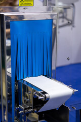 Close-up view of empty white narrow conveyer belt and blue curtain of x-ray inspecting machine in industrial building. Soft focus. Copy space. Manufacturing and production line theme.