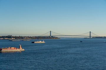Fototapeta premium ships sailing towards Verrazzano-Narrows Bridge with urban architecture and sky in the background