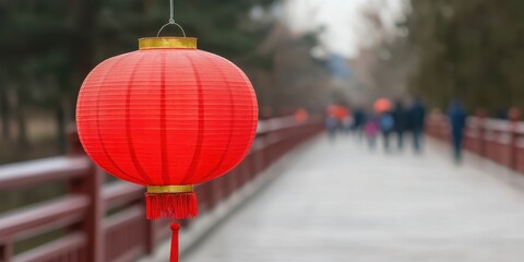 Obraz premium A vibrant red lantern hanging near a pathway, with blurred figures walking in the background, suggesting a festive atmosphere.