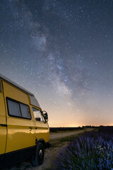 Retro yellow camper van parked under the starry sky in Valensole lavender fields in Provence, France. Long exposure astrophotography