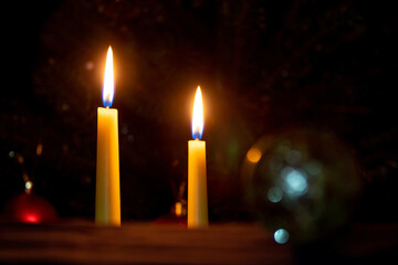 two lit candles near the Christmas tree on a dark background