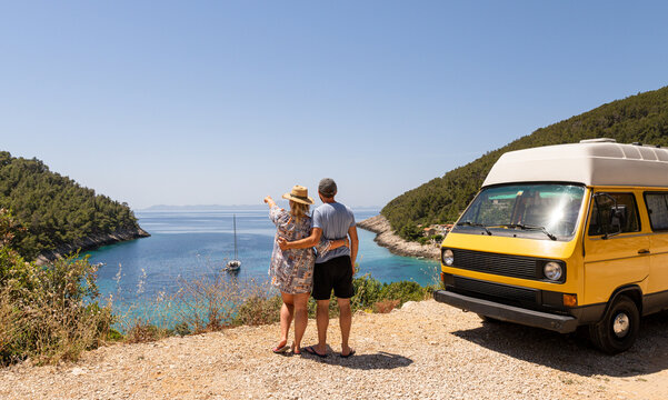 Couple enjoying the sea view on Pupnatska Luka beach standing by their retro yellow camper van parked on a cliff, Korcula island, Croatia