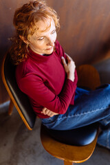 Pensive woman sitting in chair with thoughtful expression indoors