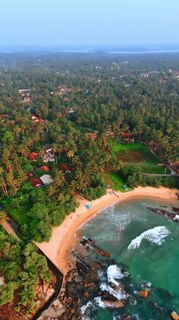 Beautiful sandy beach with multiple rocks sticking out of the water. Numerous cottages located among the lush tropical forests. Vertical video.