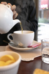 Pouring Hot Tea from Teapot into Cup at Cozy Café for Relaxing Morning Ritual