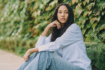 A young woman poses gracefully outdoors, surrounded by lush foliage, enjoying the serene moment