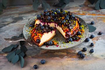 Homemade cheesecake with blueberries and green pistachios served as close-up on a Nordic design plate