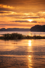 Sunrise idyll landscape on a river with a cloudy sky at golden hour