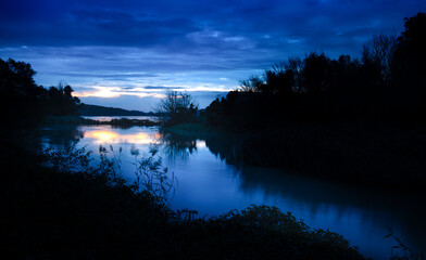 Sunrise idyll landscape on a river with a cloudy sky at blue hour