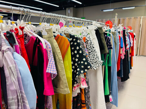Clothing on hangers, on rails in a second-hand store. Colored clothes display in market. Huge selection of different used clothes for men, women and children on the rack in thrift store.