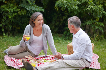 Park, mature couple and picnic with food for nutrition, hungry and bonding together with communication. Happy people, man and woman with juice glass for drinking, beverage and commitment in marriage