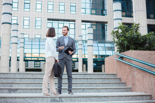 Successful young male and female businesspeople standing and talking on the stairs in front of an office building.
