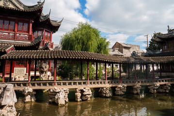 Yuyuan Garden in Shanghai features a covered walkway with wooden carvings, a pond with rock formations, lush greenery, and traditional buildings.