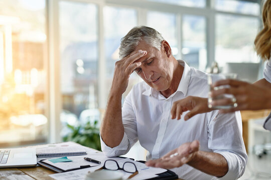Business, headache and medicine for mature man in office with help from assistant or employee. Glass, pill or stress and overworked corporate manager in workplace with symptoms of burnout migraine