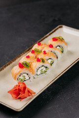 Close-up of sushi rolls with salmon, cream cheese, and cucumber, garnished with wasabi and roe