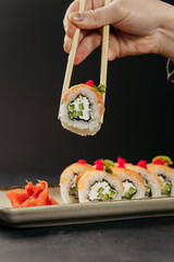 Hand holding sushi roll with salmon, cucumber, and cream cheese using chopsticks