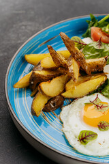 Breakfast plate with fried eggs, roasted potatoes, fresh salad, and sardine toasts on a blue dish