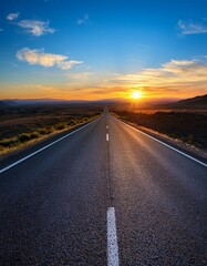 A long, straight road stretches out into the distance, leading towards a brilliant sunset over the horizon. 