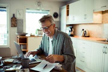 Senior mature man using laptop on kitchen table