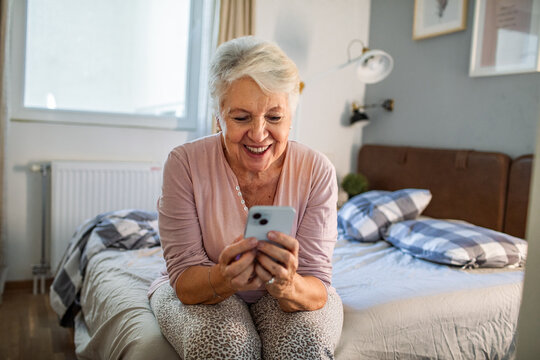 Smiling senior woman using smartphone on the bed at home