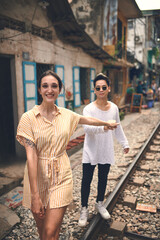 Couple, portrait and smile with walking on train tracks in Vietnam for travel adventure, local experience or love. Tourist attraction, interracial people and holding hands on railroad for sightseeing