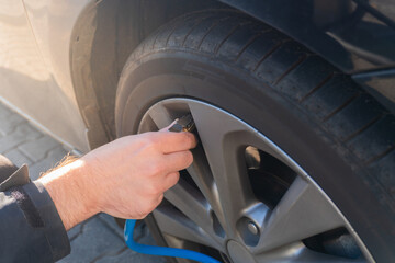 A close-up of a driver’s hand inflating his car’s tire, monitoring pressure levels for optimal performance and reliability. By focusing on tire care, he ensures smooth driving.