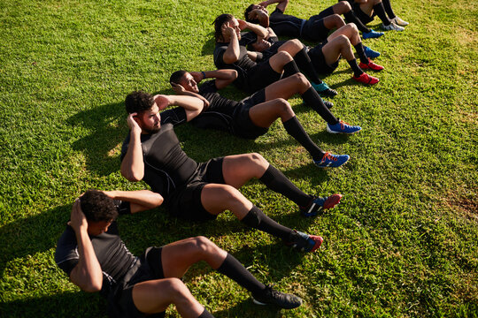 Men, rugby and sit ups with team on grass field for training, practice or outdoor workout for game or match. Active, group or football players in sport, line or row for fitness, crunches or warm up