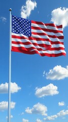 Obraz premium A large American flag is flying in the sky. The flag is blue, white, and red. The sky is clear and blue, with a few clouds scattered throughout. The flag is waving in the wind
