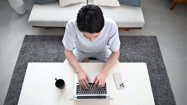 Video of a fresh image of a handsome man typing on a computer in a beautiful living room Overhead view