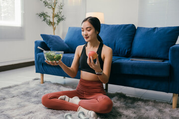 Sitting on a rug in her living room, a young woman in sportswear contemplates her healthy food choices, holding a bowl of fresh salad and an apple, promoting a balanced diet and mindful eating