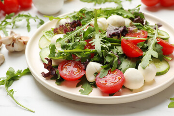 Tasty salad with arugula, lettuce, mozzarella cheese and vegetables on white table, closeup