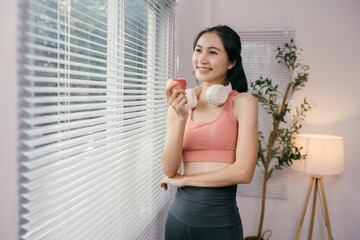Young asian woman in sportswear is enjoying a healthy snack of an apple after exercising at home, promoting a healthy and active lifestyle