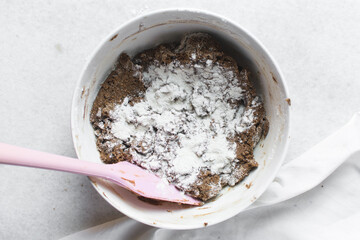 Overhead view of flour being mixed into molasses cookie dough, top view of gingerbread cookie dough in a white mixing bowl, process of making christmas cookies