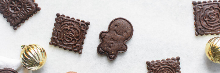 Overhead view of stamped molasses cookies and gold Christmas ornaments on a parchment lined baking tray